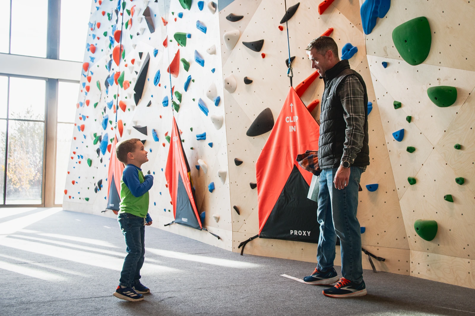 A Person And A Boy Standing Next To A Climbing Wall